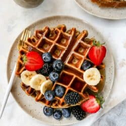 Protein waffle topped with berries and maple syrup on a plate.