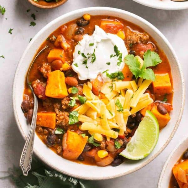 A bowl of sweet potato chili topped with shredded cheese, sour cream and a lime wedge.