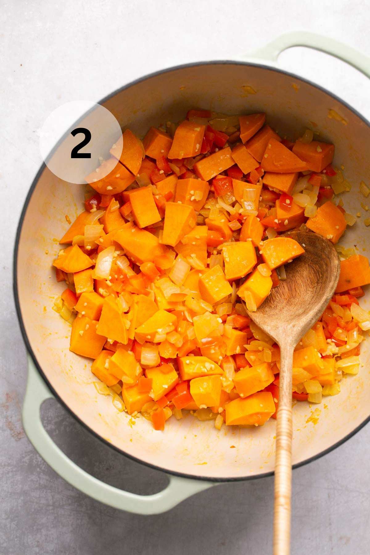 Using a wooden spoon to stir cubed sweet potato with sautéed veggies.