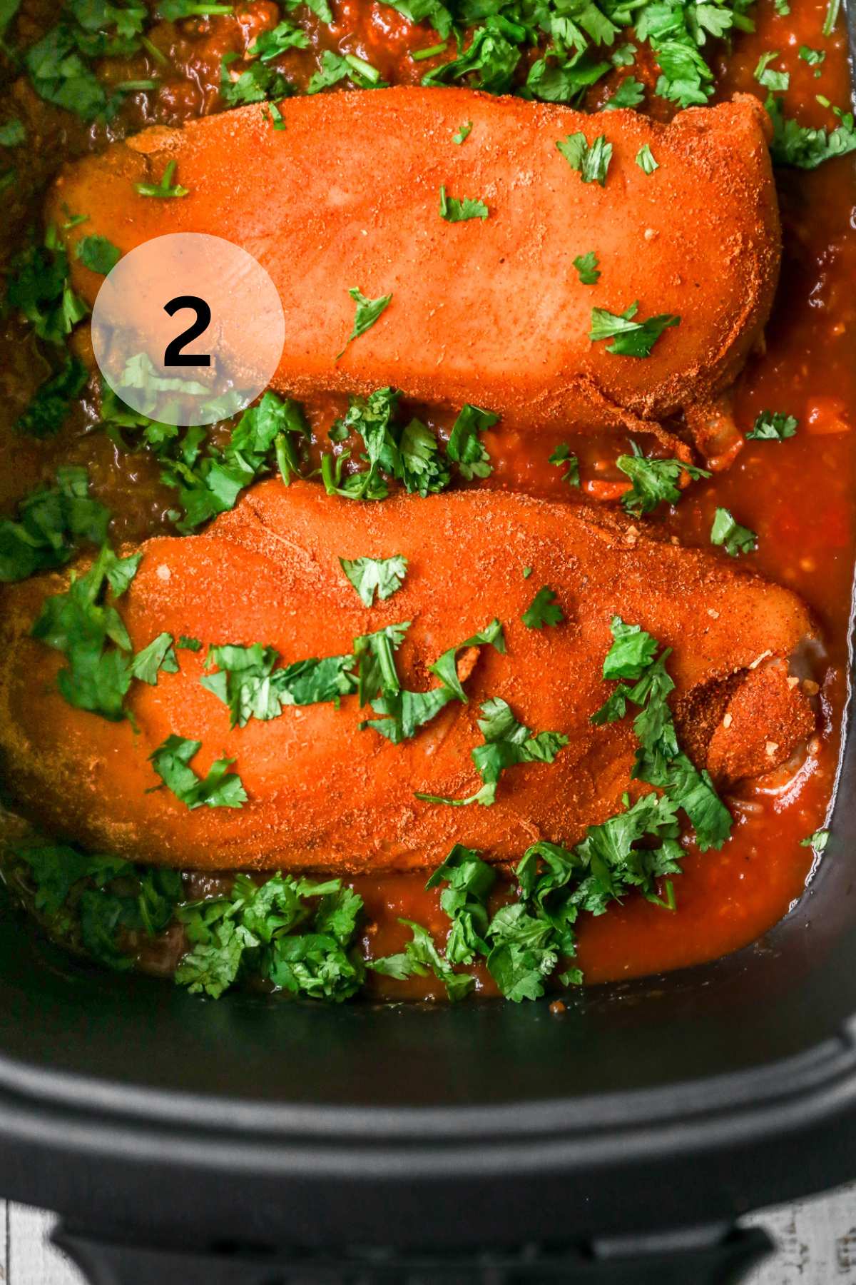 Chicken breasts in a slow cooker topped with fresh cilantro.