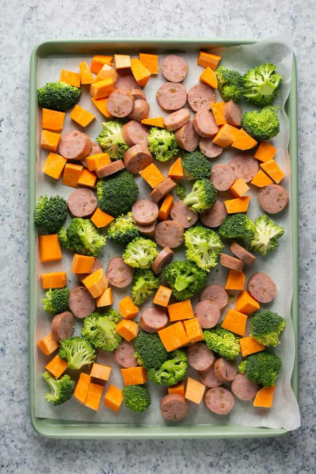 Uncooked sausage and veggies on a parchment-lined sheet pan.