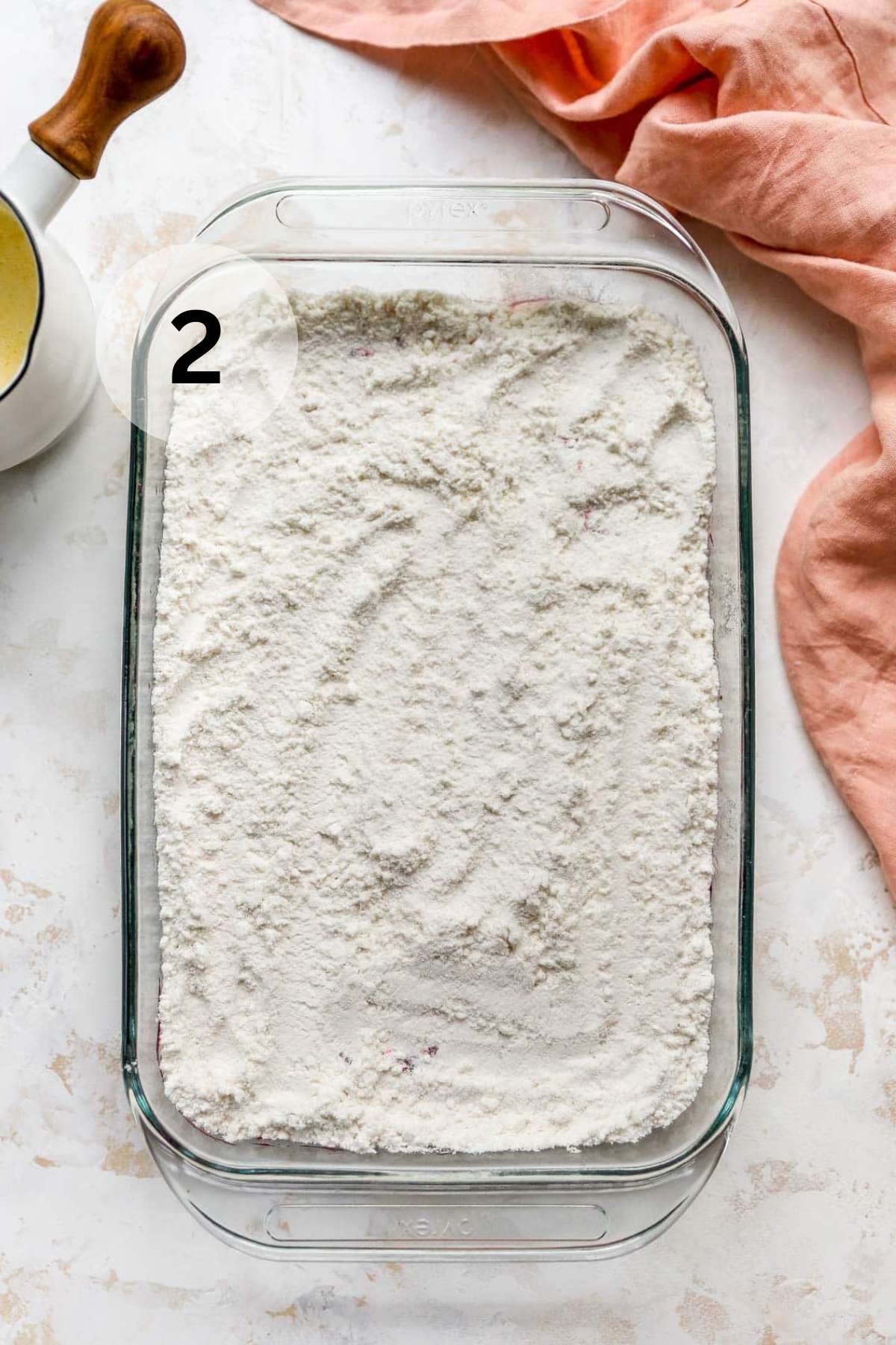 Yellow cake mix over cherry pie filling in a glass baking dish.