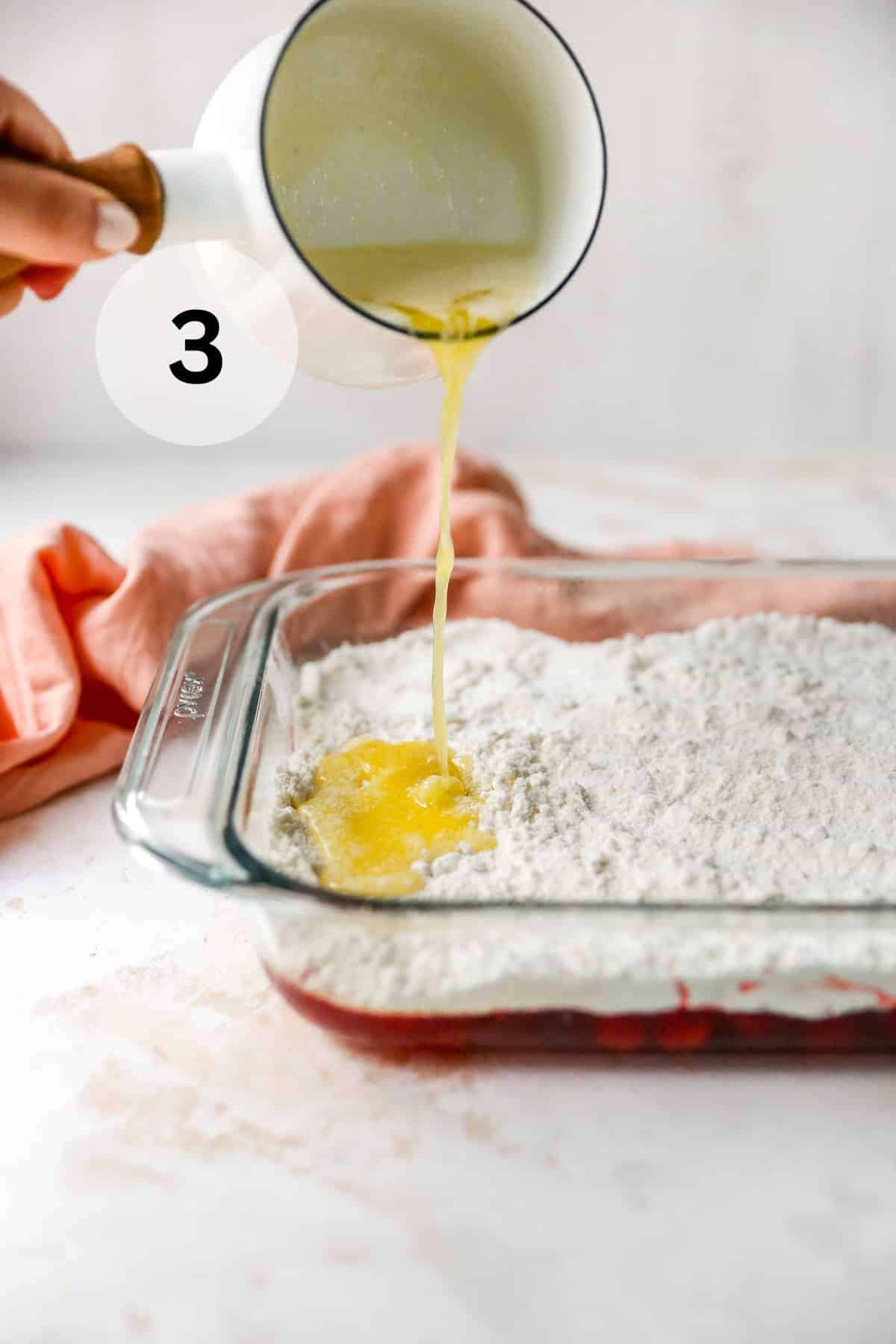 Pouring melted butter over the top of a layer of dry cake mix.