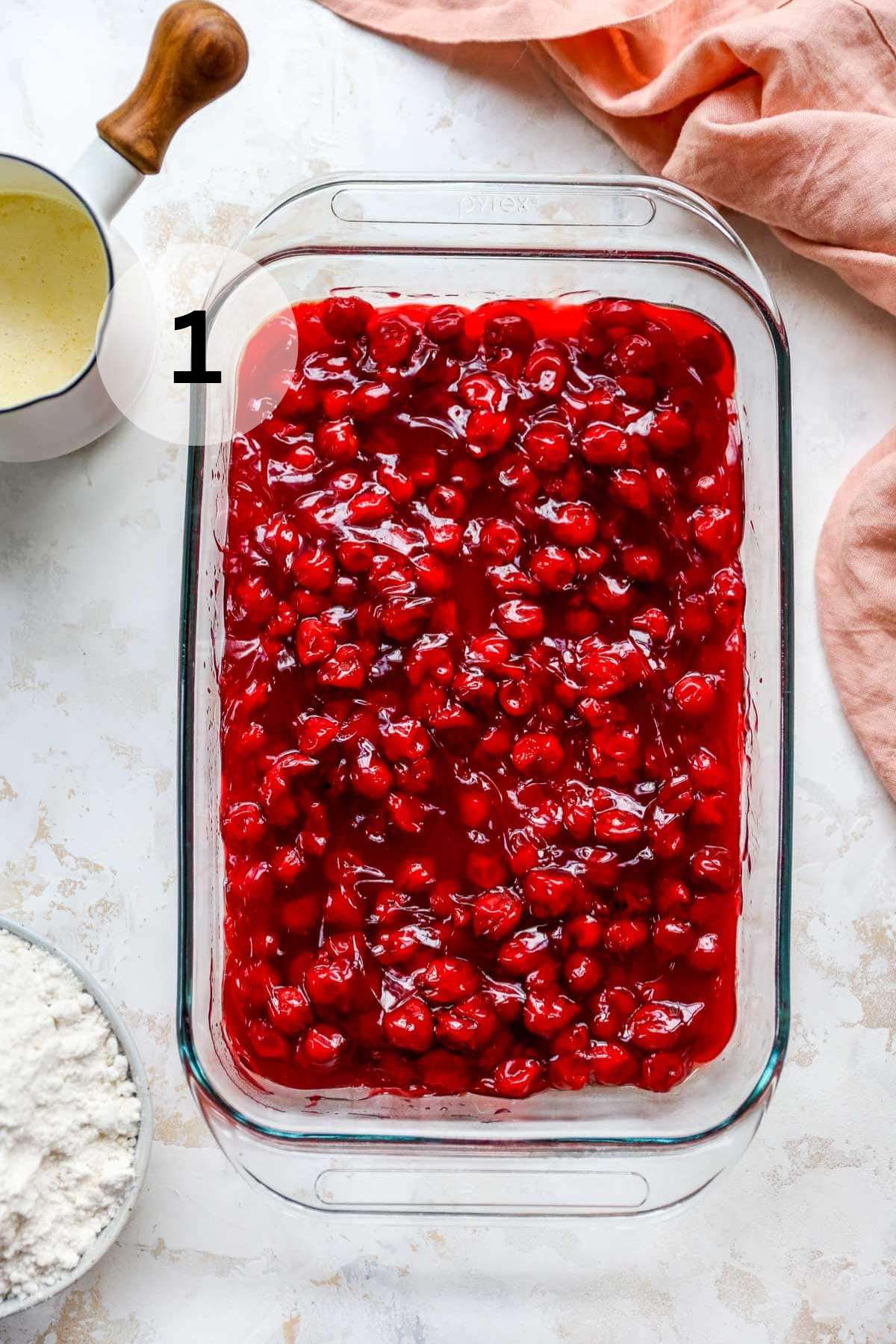 Adding cherry pie filling to a glass dish.