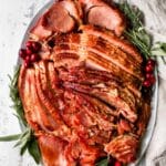 Slow cooker ham on serving platter garnished with herbs and berries.