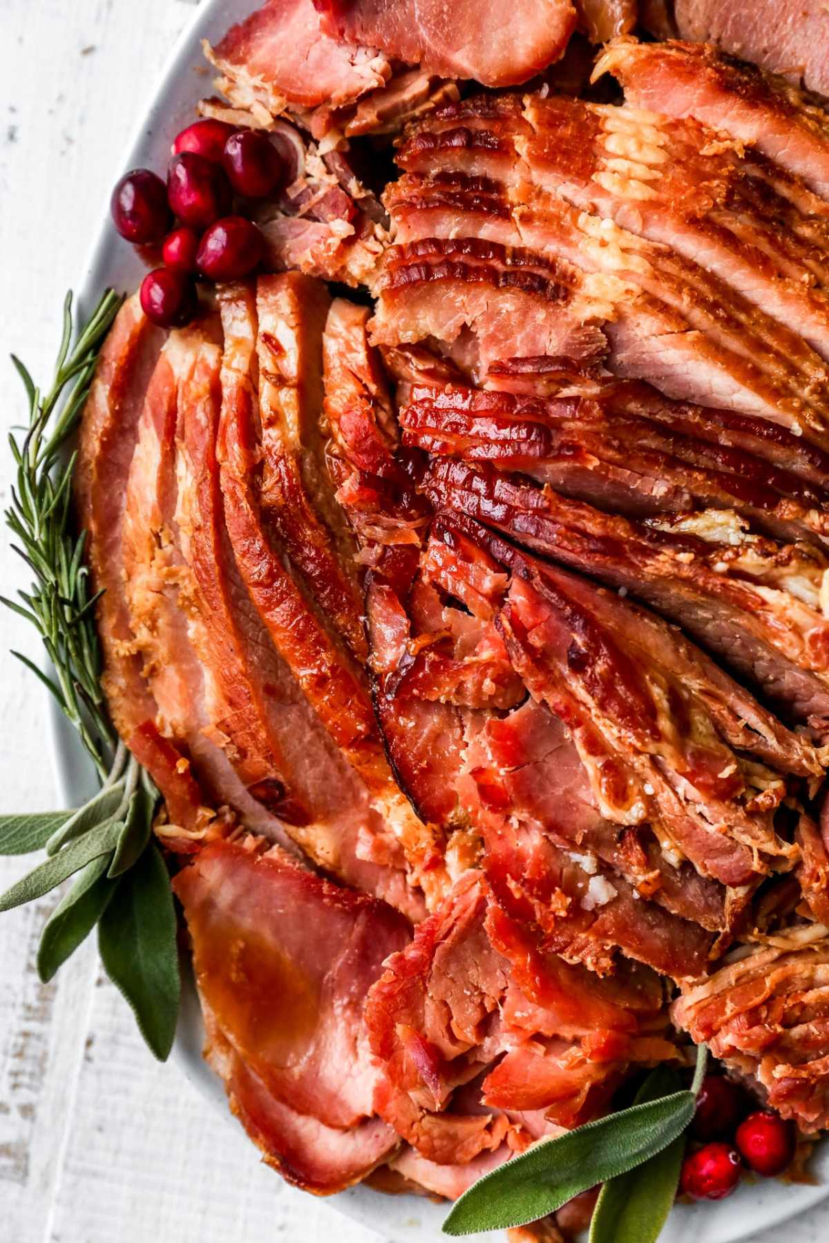 Sliced ham on a tray garnished with sage and rosemary.