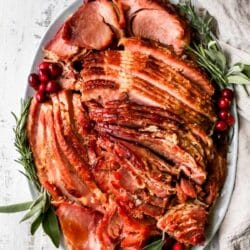 Slow cooker ham on serving platter garnished with herbs and berries.