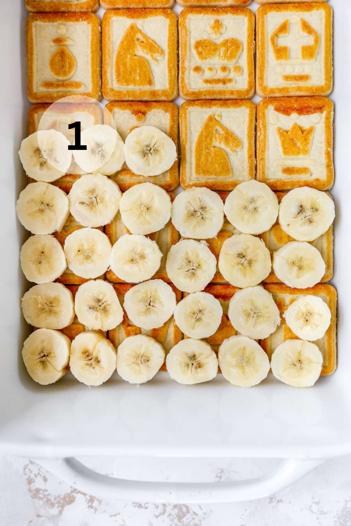 Placing banana slices over Chessman butter cookies in a white dish.