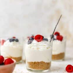 Small glasses with a layer of graham cracker crust, cheesecake and berries.