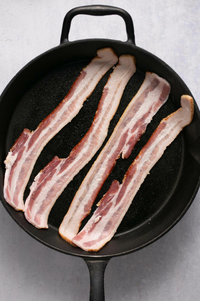 Slices of raw bacon in a cast iron skillet.