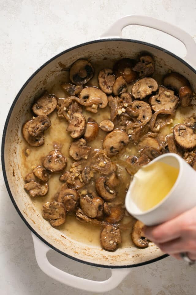 Pouring chicken broth in a pan with mushrooms.