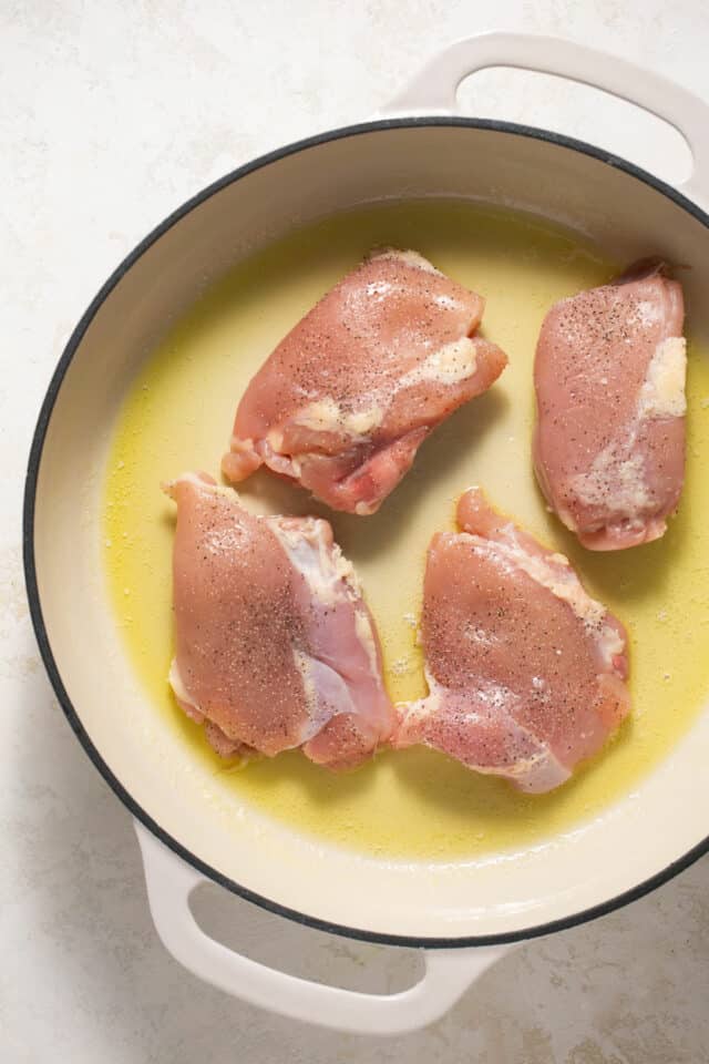 Raw chicken thighs in a pan with melted butter.