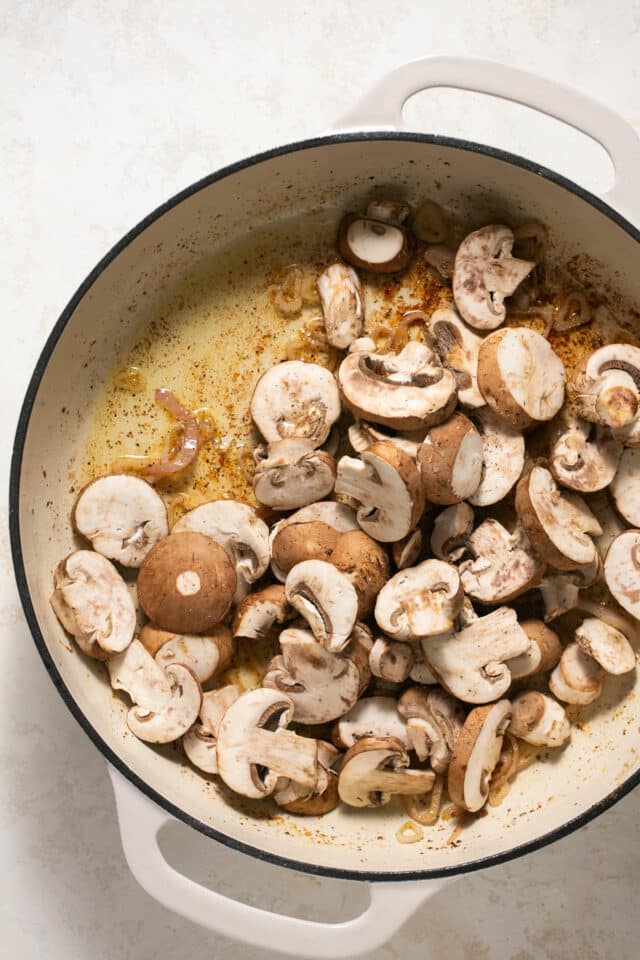 Adding mushrooms to a pan with butter.