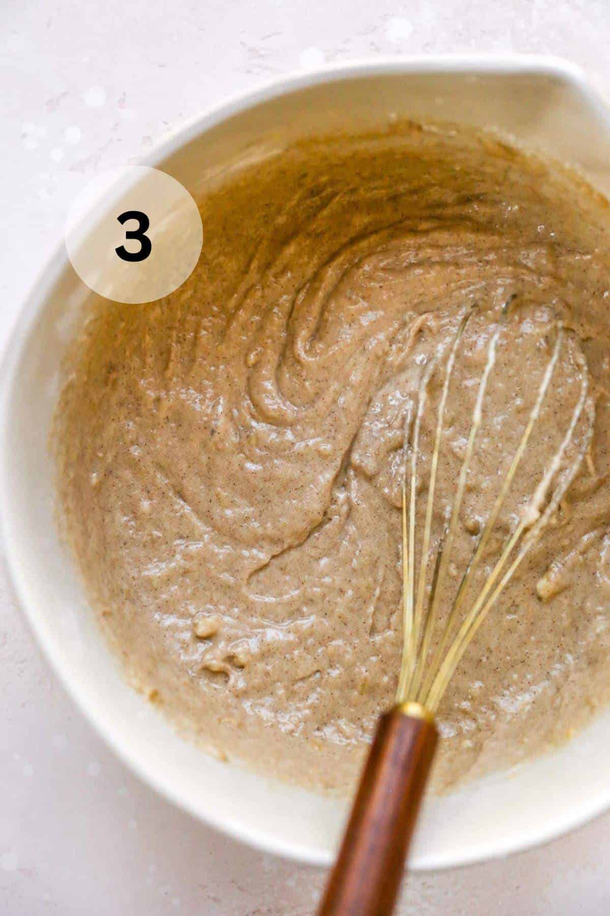 A whisk in a bowl with muffin batter.