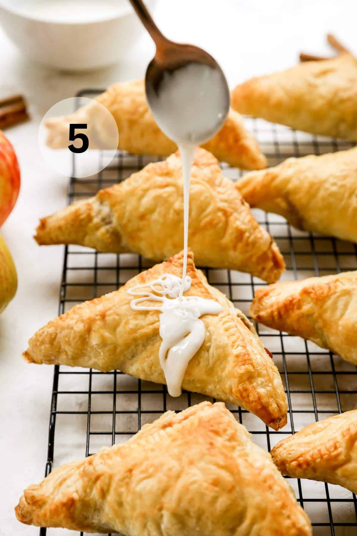 Drizzling glaze over an apple turnover on a wire rack.