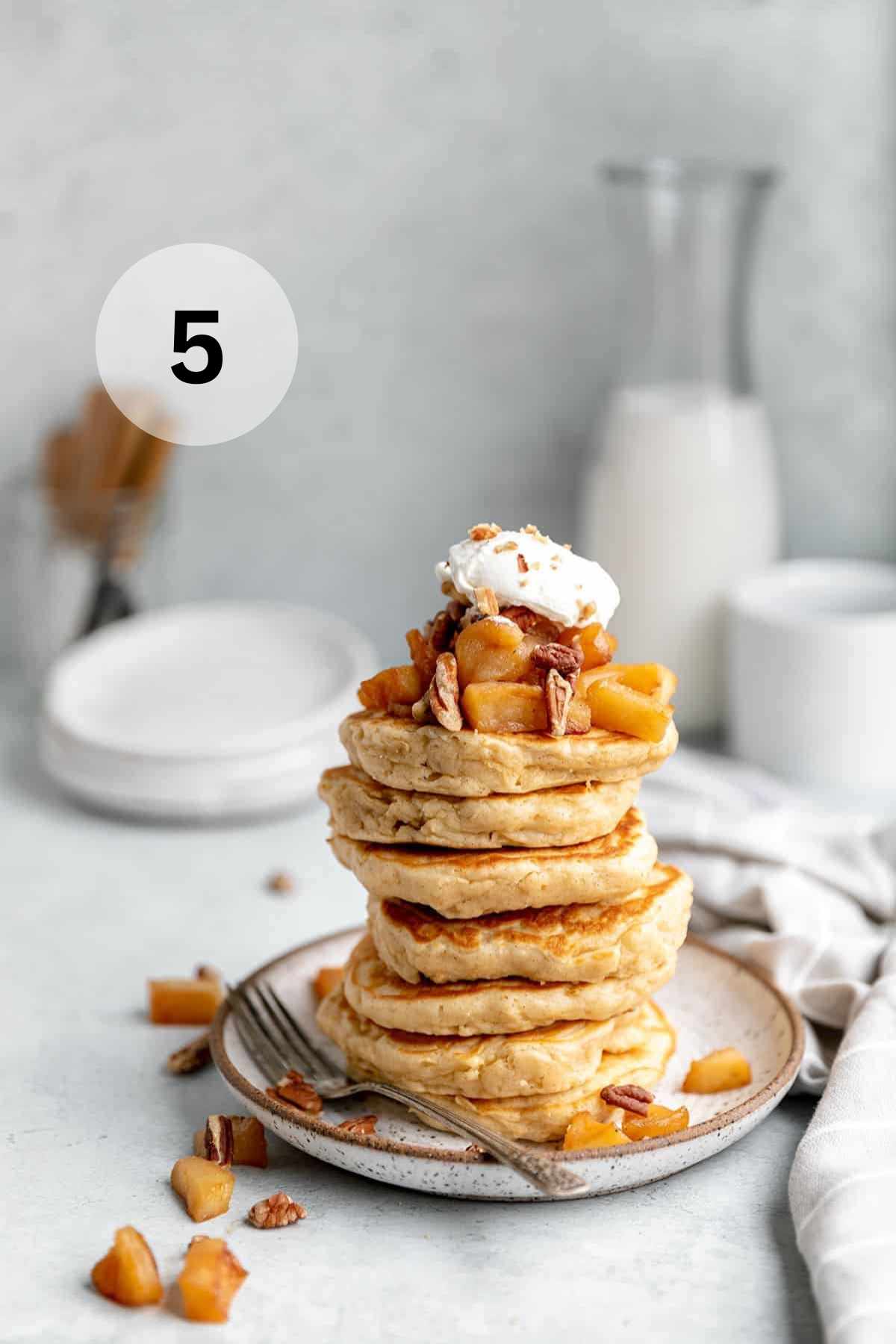 Stack of pancakes topped with apples and whipped cream.