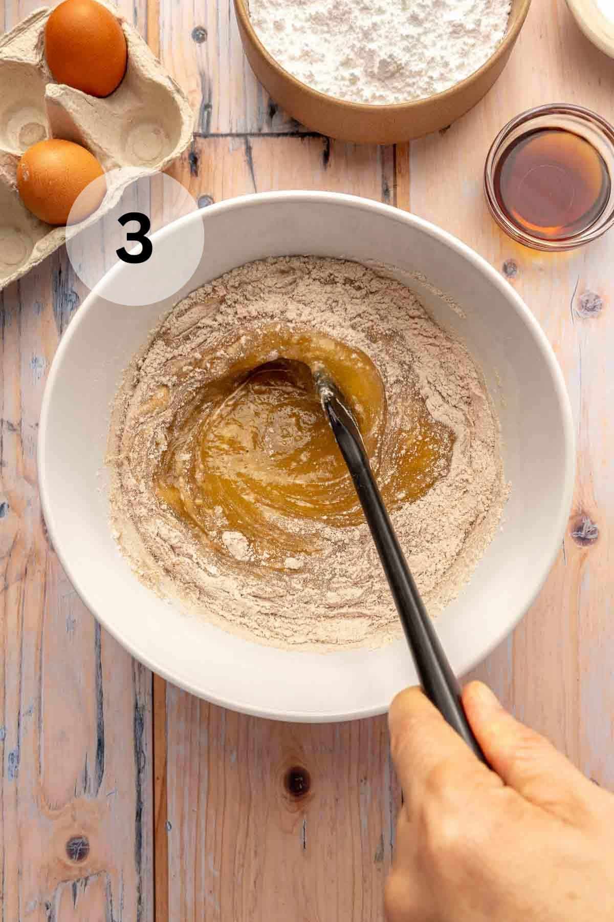 Stirring together wet and dry ingredients in a white bowl.