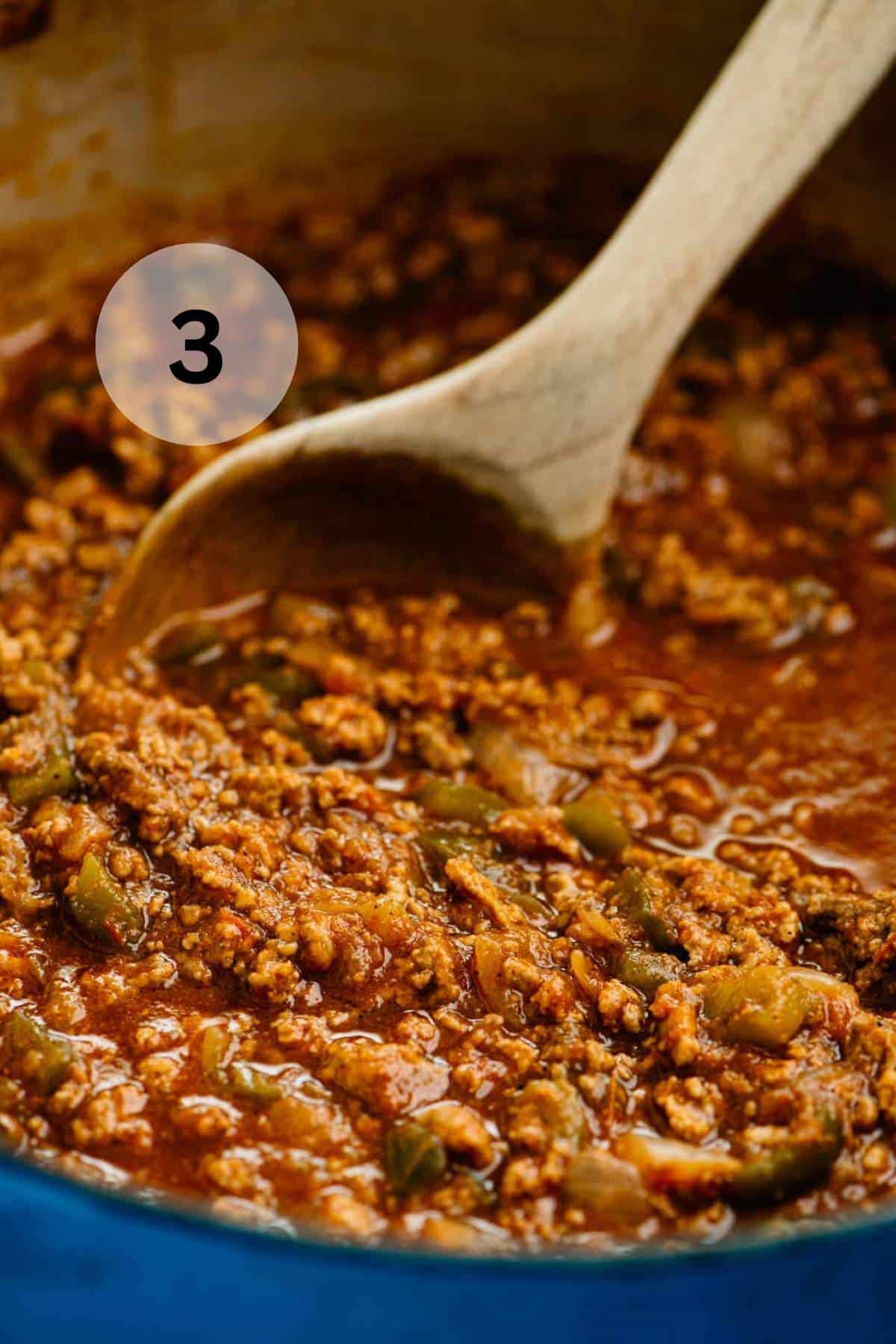 Stirring beef chili with a wooden spoon.