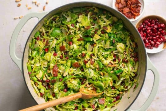 Stirring shaved brussel sprouts with bacon, almonds and pomegranate seeds.