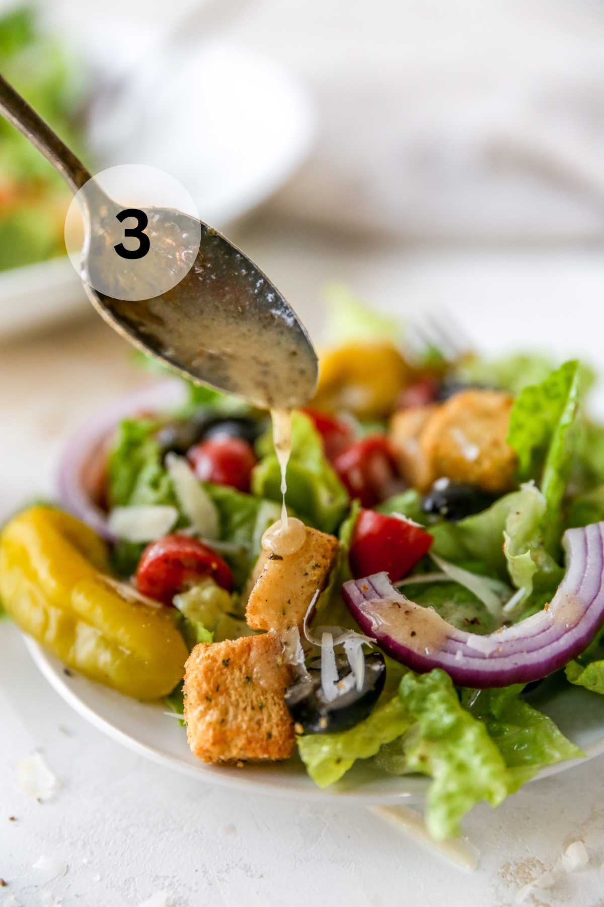 Drizzling dressing over a salad with a spoon.