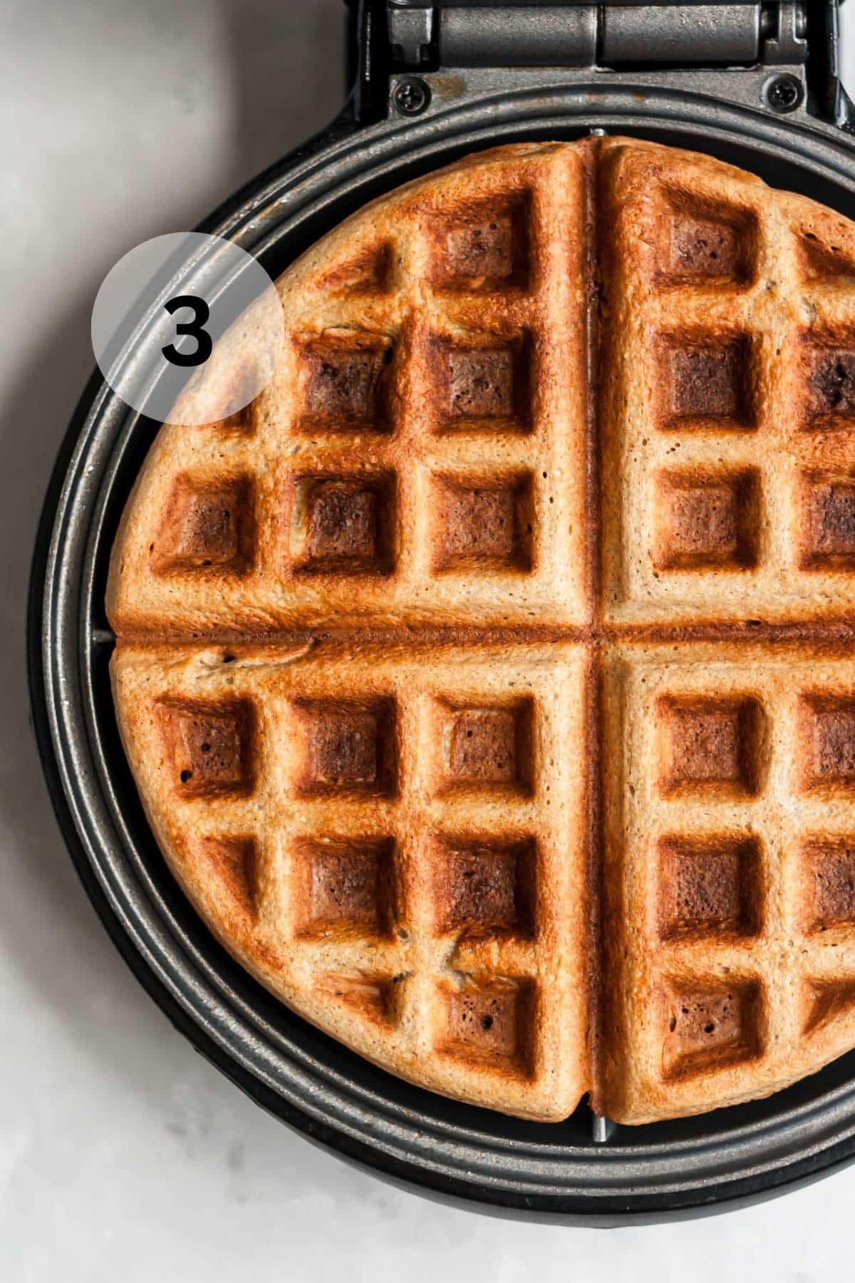 A waffle cooking in a waffle maker.