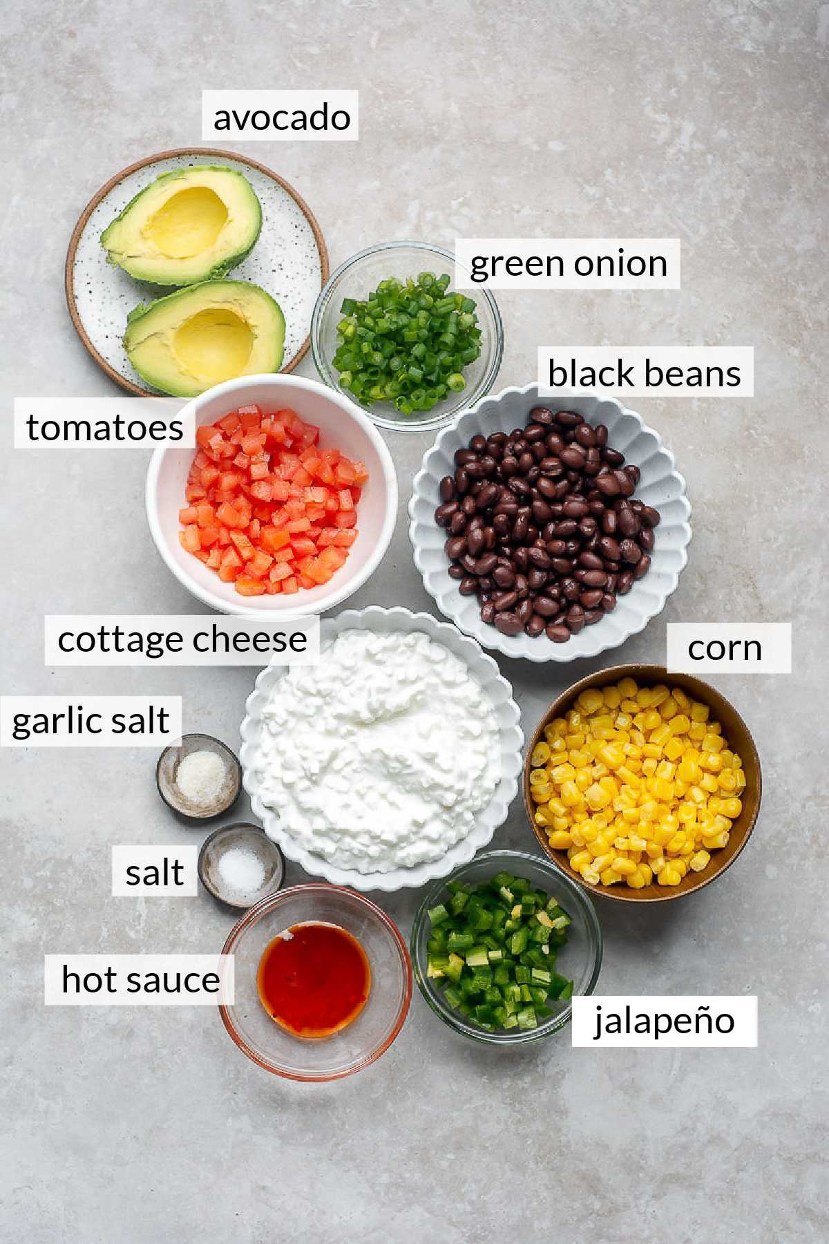 Small bowl of black beans, corn, cottage cheese, tomatoes, avocado, green onions and sriracha sauce.