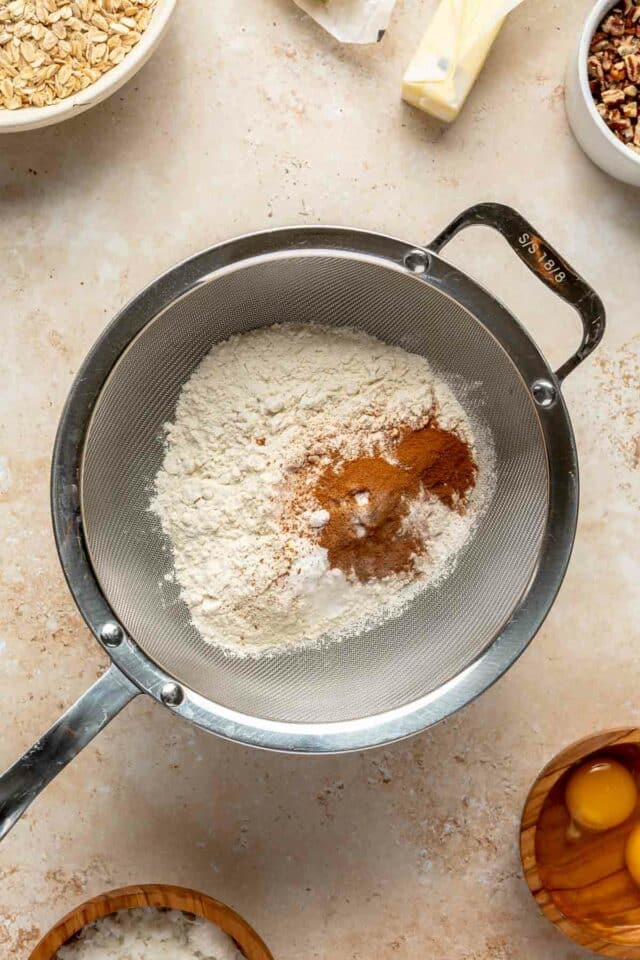 Sifting cinnamon with flour, baking powder, baking soda and salt.