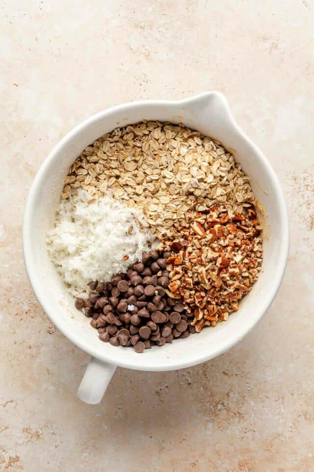 Chocolate chips, chopped pecans and coconut added to large white bowl.
