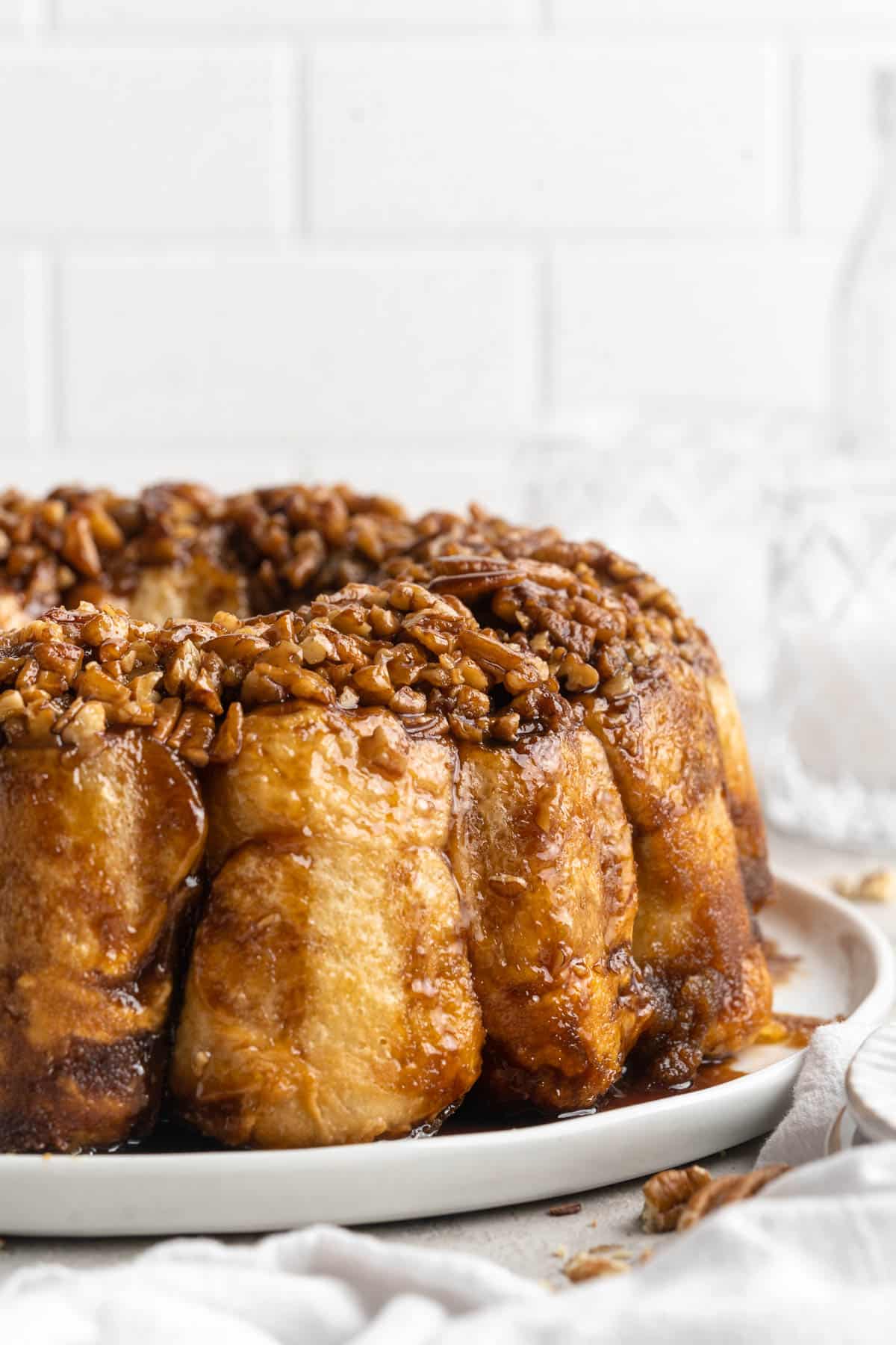 Monkey bread topped with chopped pecans on a white plate.