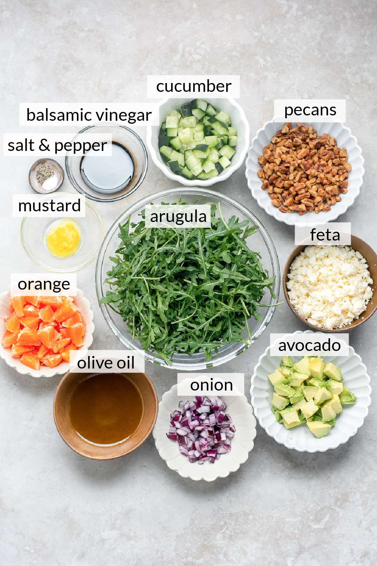 Small bowls with arugula, cucumber, pecans, feta, avocado, orange slices and red onion.