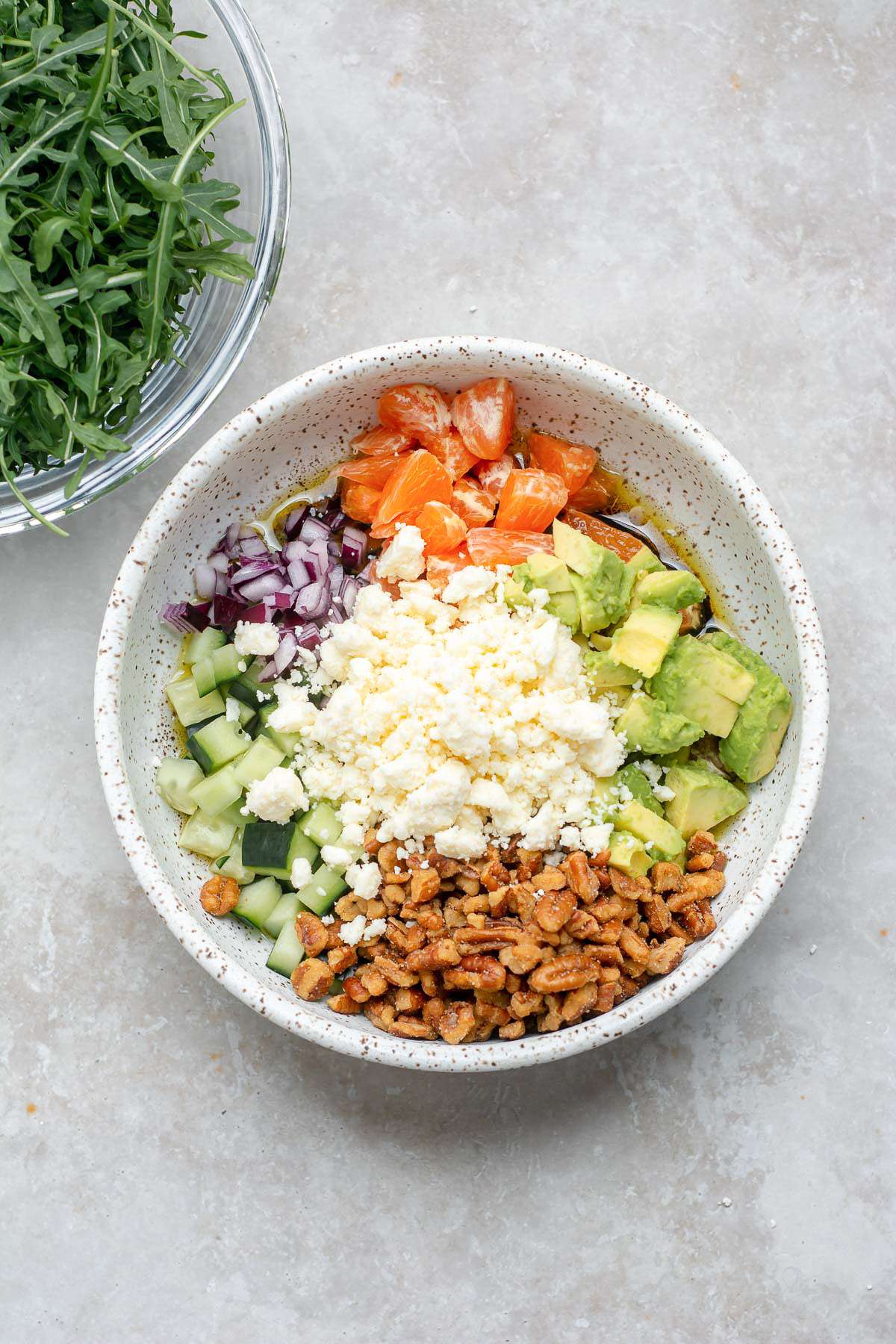 Feta cheese in a bowl with chopped pecans, orange, cucumber and red onion.