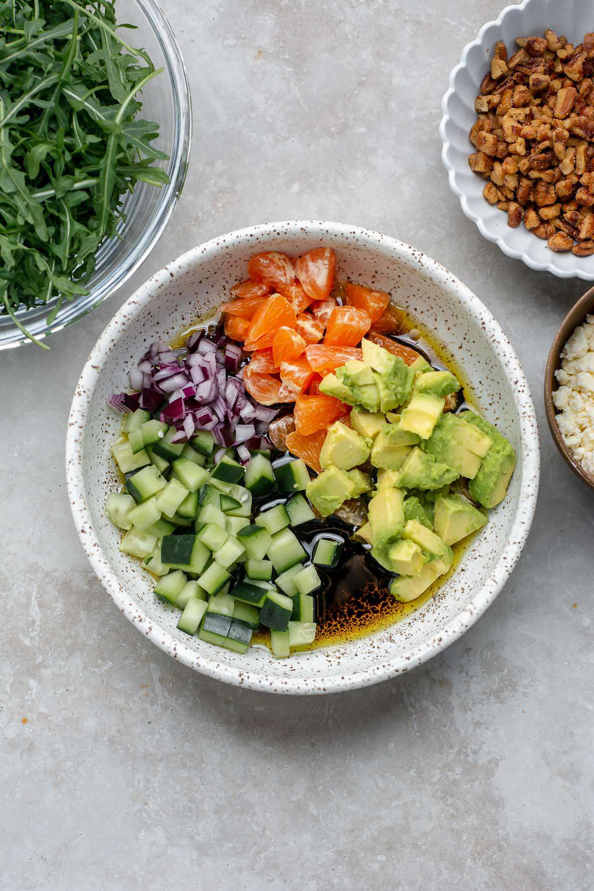 Chopped cucumber, avocado, red onion and orange in a bowl with dressing.