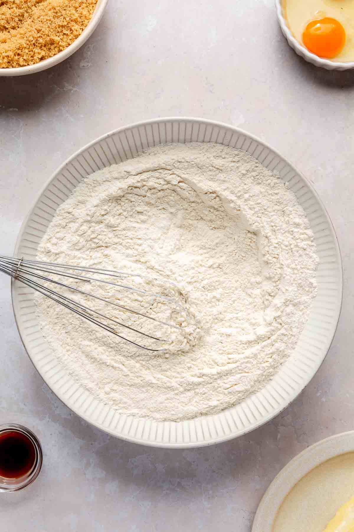 Using a whisk to mix flour with other dry ingredients in a bowl.