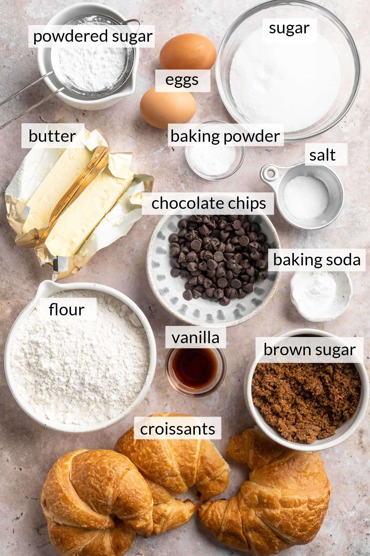 Croissants, butter, flour, sugar, chocolate chips, eggs and powdered sugar divided into small portions.