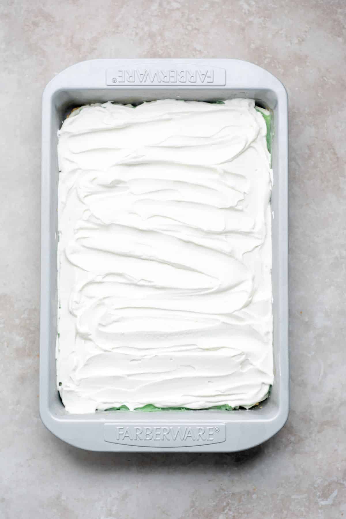 Whipped topping spread over pistachio dessert.