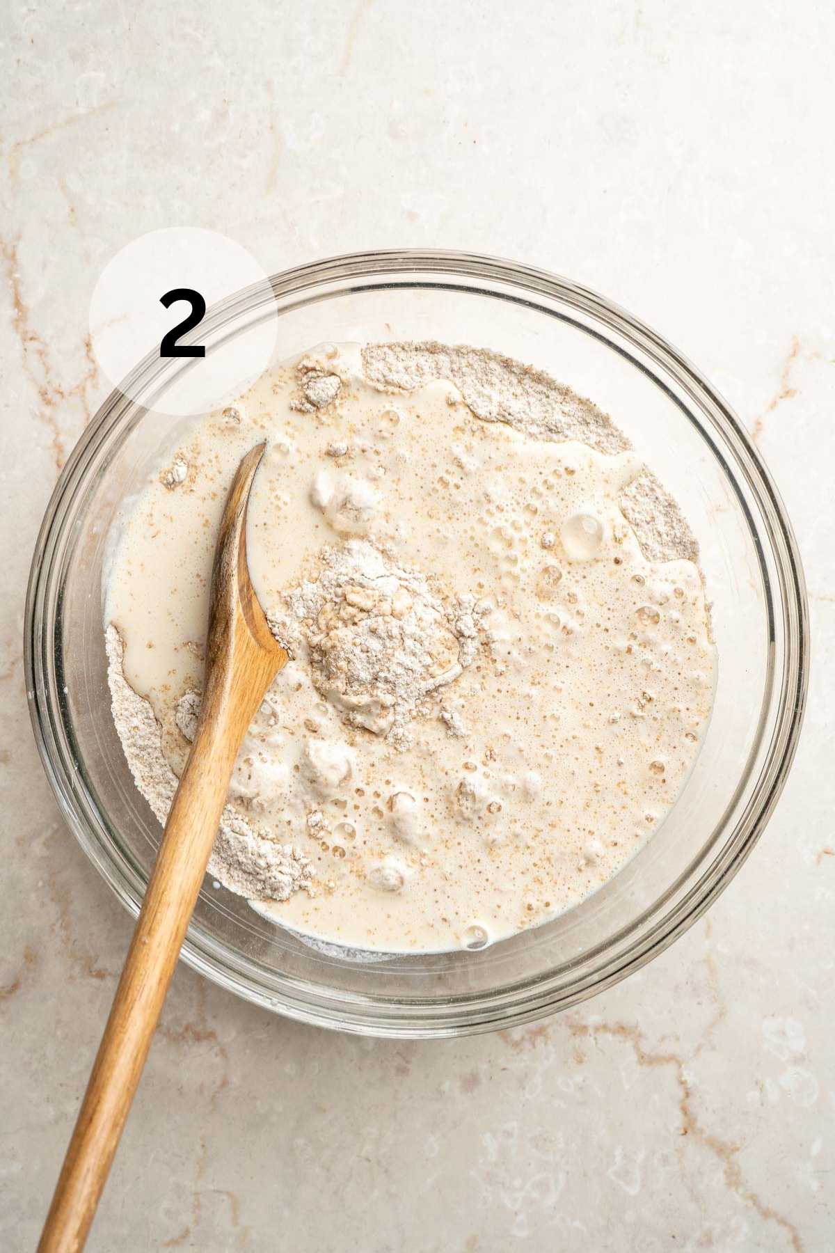 A wooden spoon stirring wet ingredients into flour mixture in a large bowl.