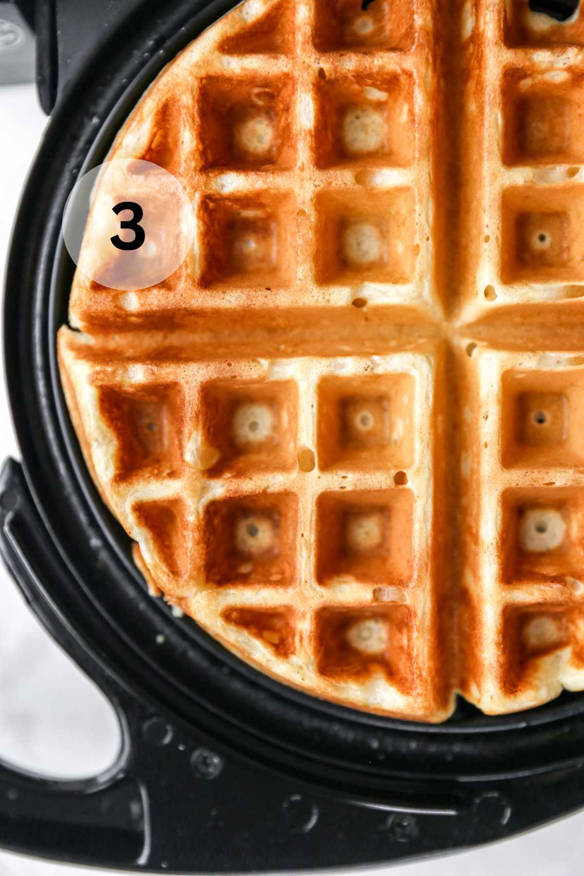 A waffle cooking in a waffle maker.