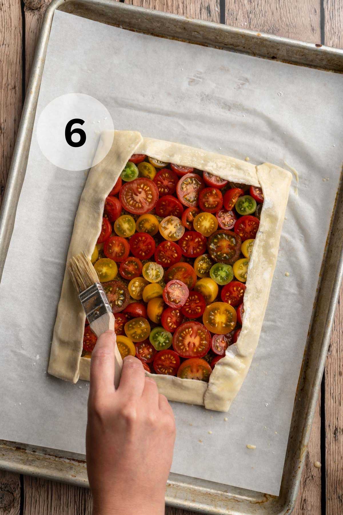 Using a pastry brush to brush sides of puff pastry with egg wash.