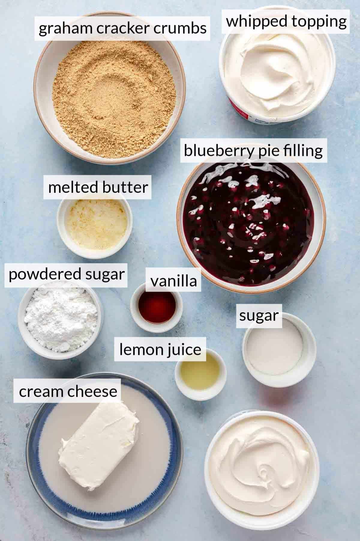 Bowls of graham cracker crumbs, blueberry pie filling, melted butter and whipped topping.