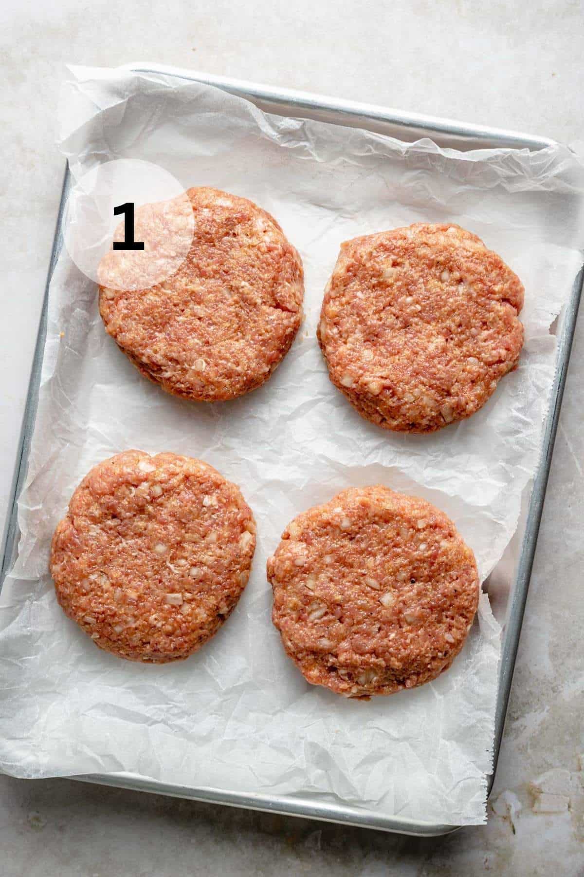 Ground chicken patties on a baking sheet lined with parchment paper.