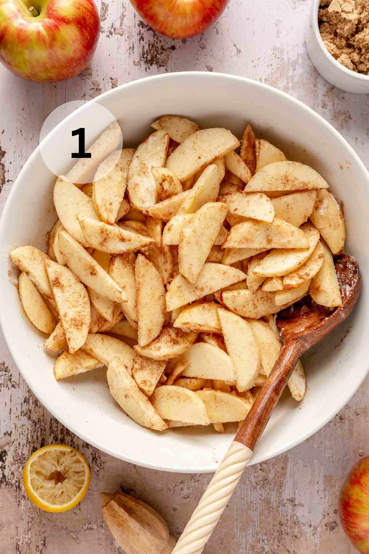 Tossing apple slices with cinnamon, sugar, flour and lemon juice in a white bowl.