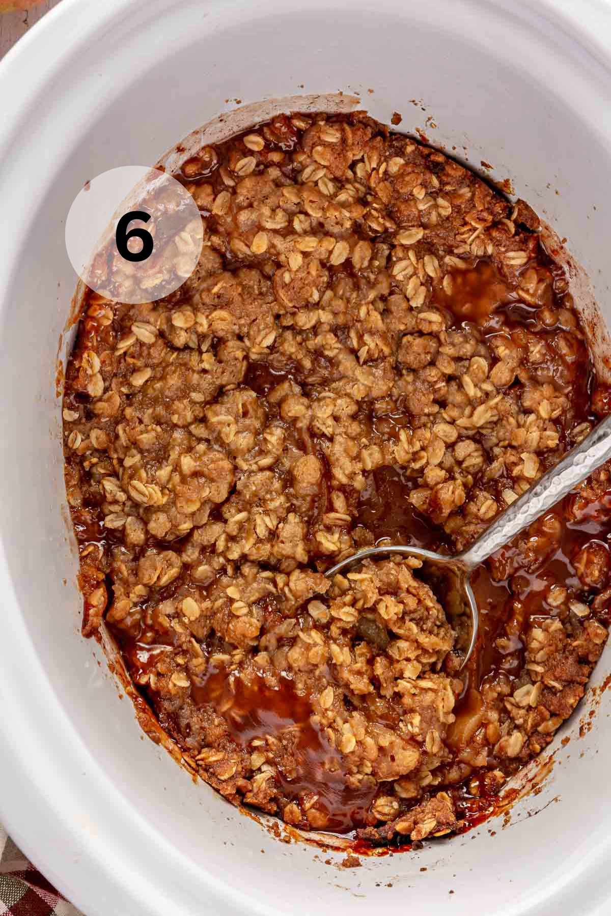 Using a serving spoon to scoop out slow cooker apple crisp.