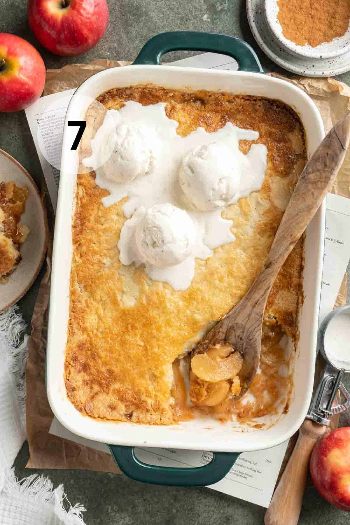 Serving an apple dump cake that is topped with scoops of ice cream with a wooden spoon.