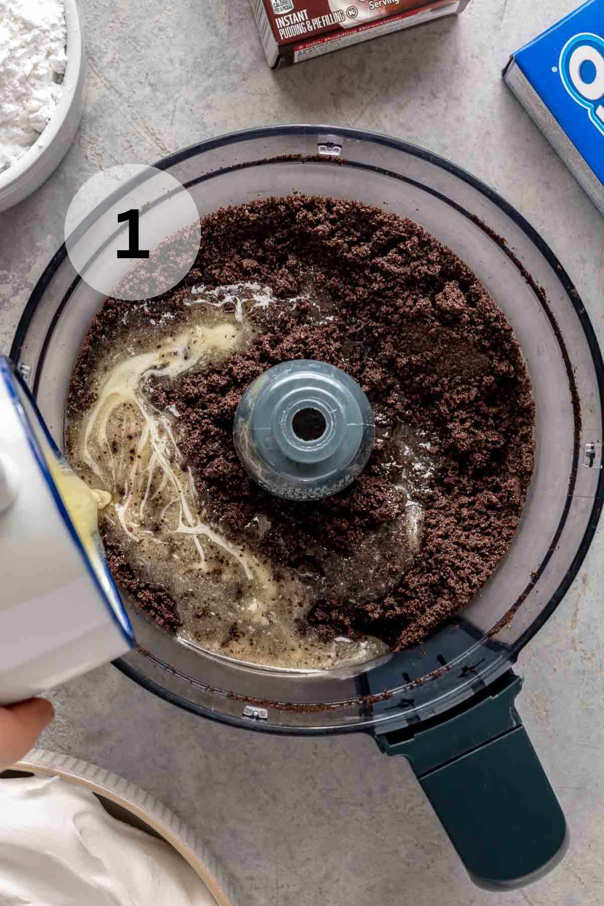 Pouring melted butter into Oreo cookie crumbs in a food processor.