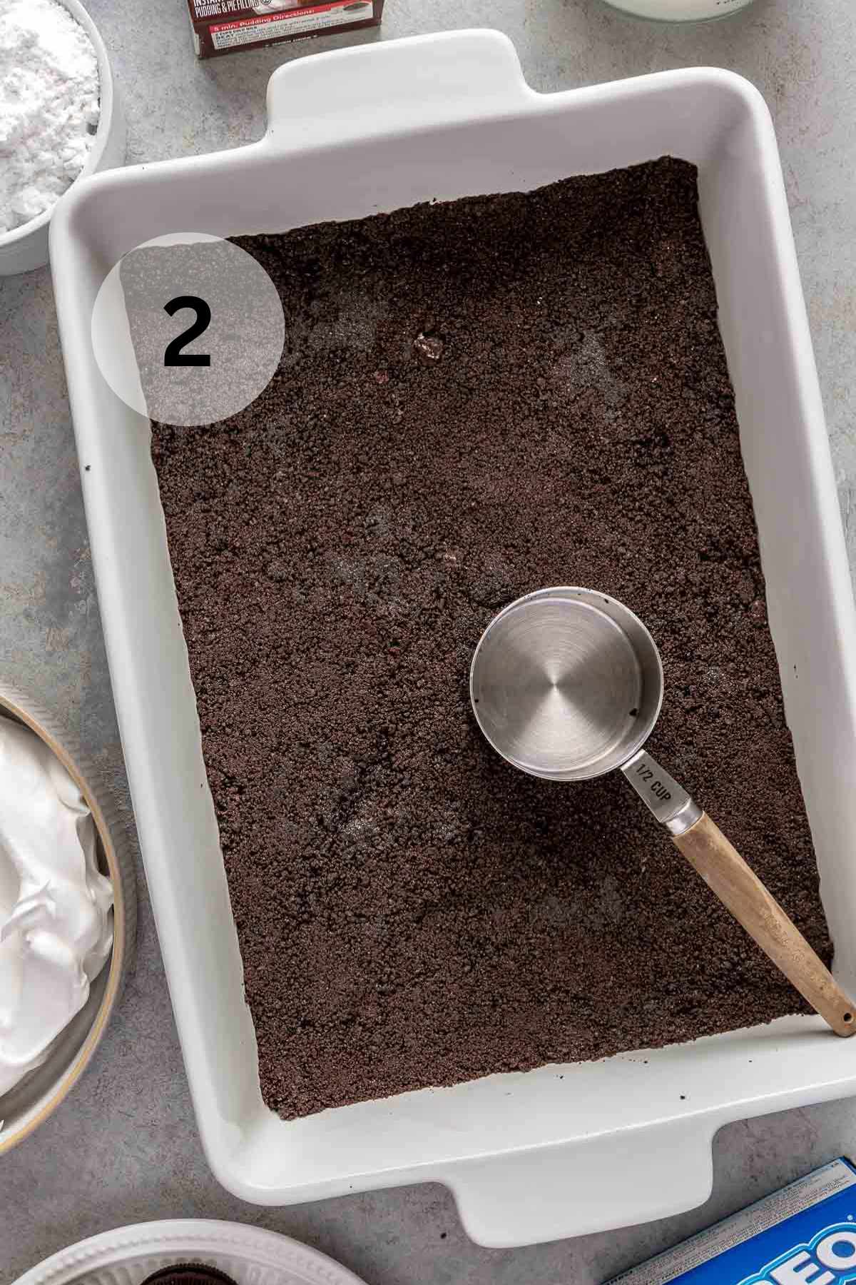 Using a measuring cup to press an Oreo crust into a pan.
