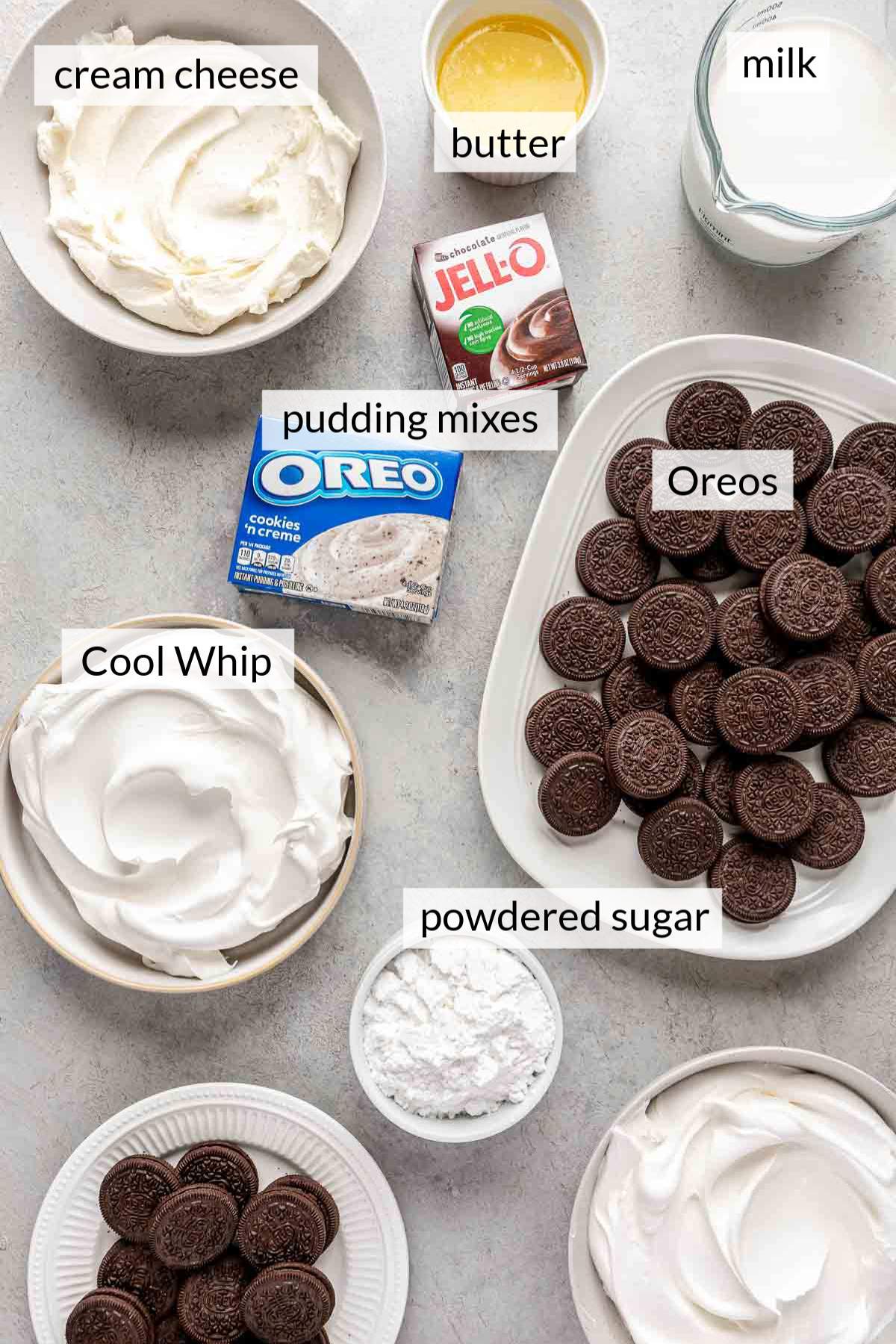 Plate full of Oreo cookies near a cup of milk, bowl of powdered sugar, butter, cream cheese and Cool Whip.