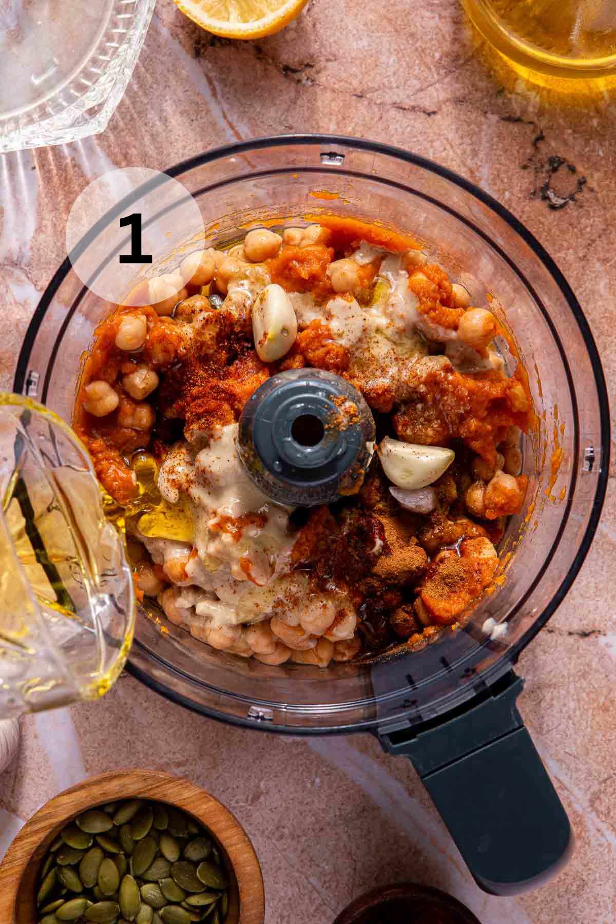Pouring olive oil into a food processor with chickpeas, spices and pumpkin puree.