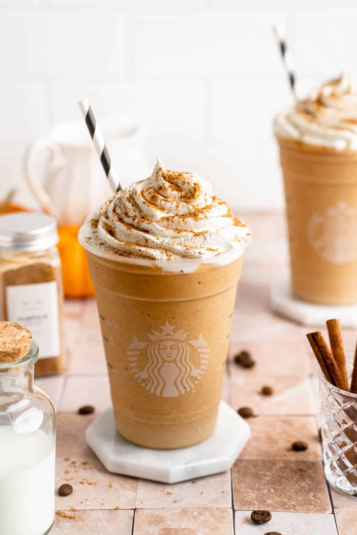 Pumpkin frappe in a Starbucks cup with a straw sitting on a tile counter.