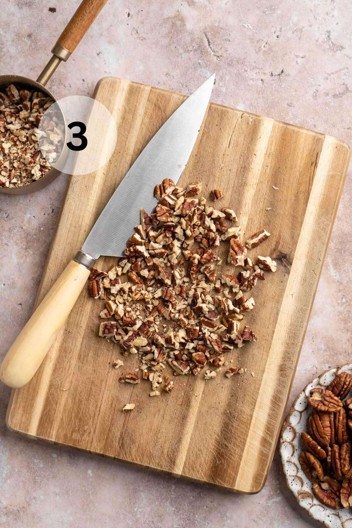 Chopped pecans on a cutting board near a sharp knife.