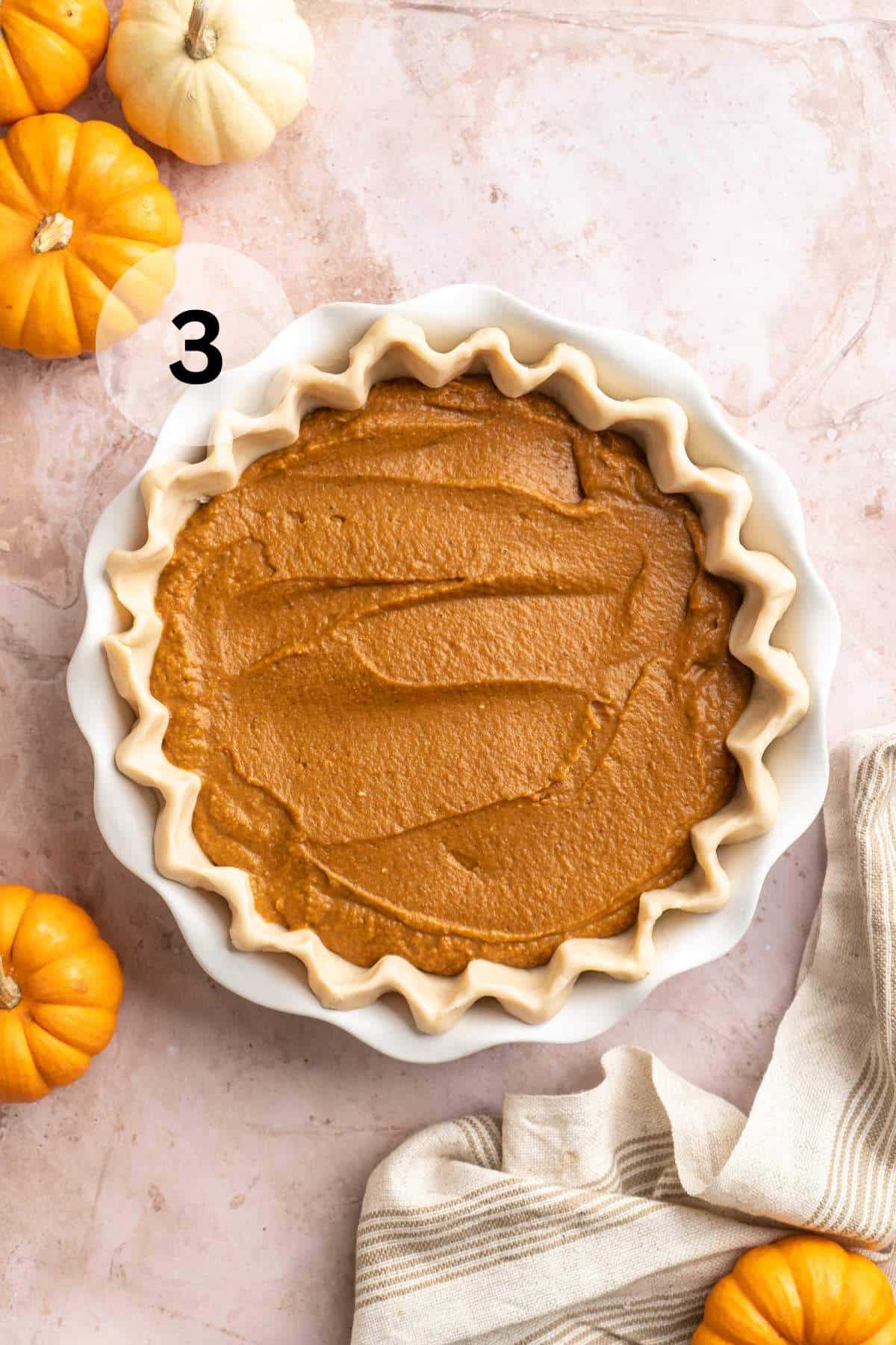 Pumpkin filling added to pie crust in a white pie plate.